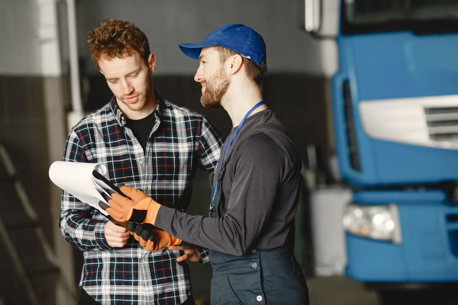 Technician in uniform consults with customer in garage setting beside a blue truck.