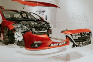 A disassembled red car with front parts and the bumper separated from the main body.