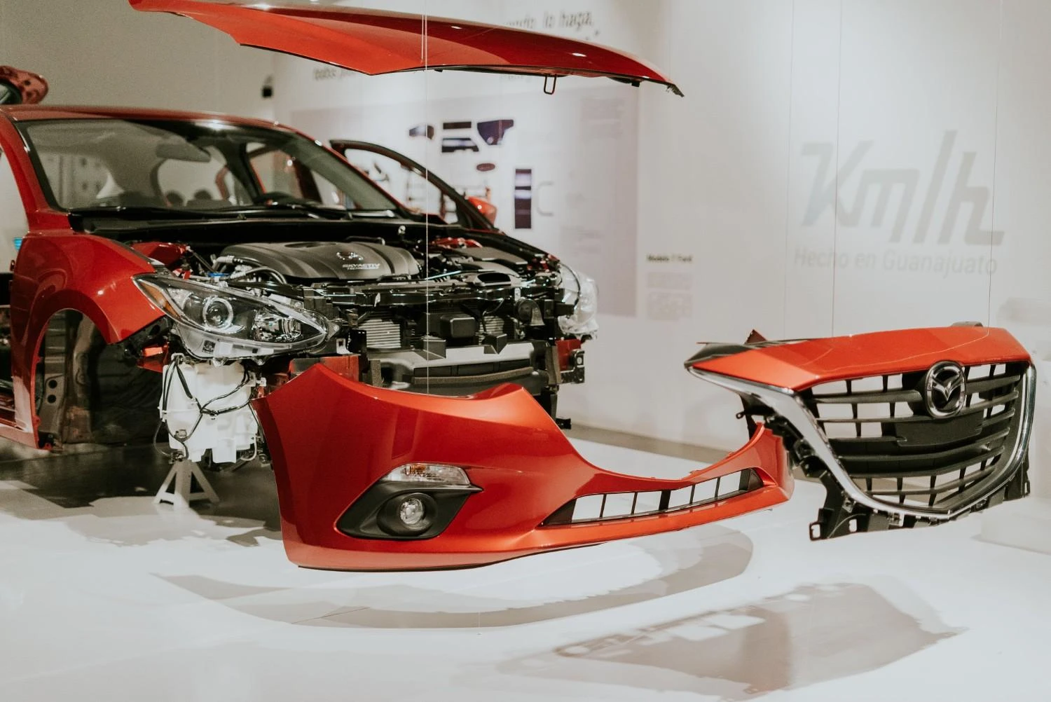A disassembled red car with front parts and the bumper separated from the main body.