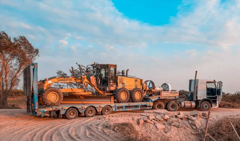 A flatbed truck tow a komatsu grader and construction equipment