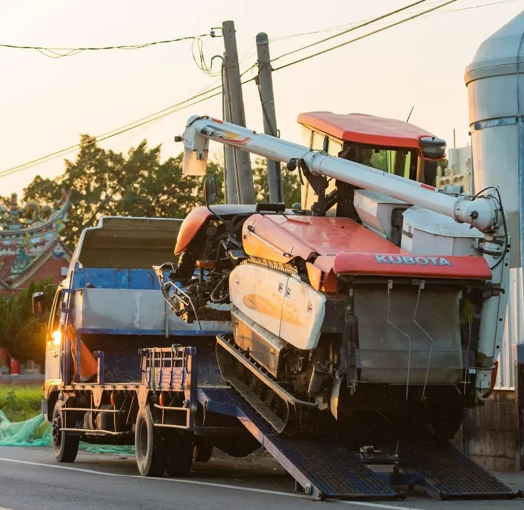 orange kubota combine harvester is being loaded onto a truck on a rural road at sunset.