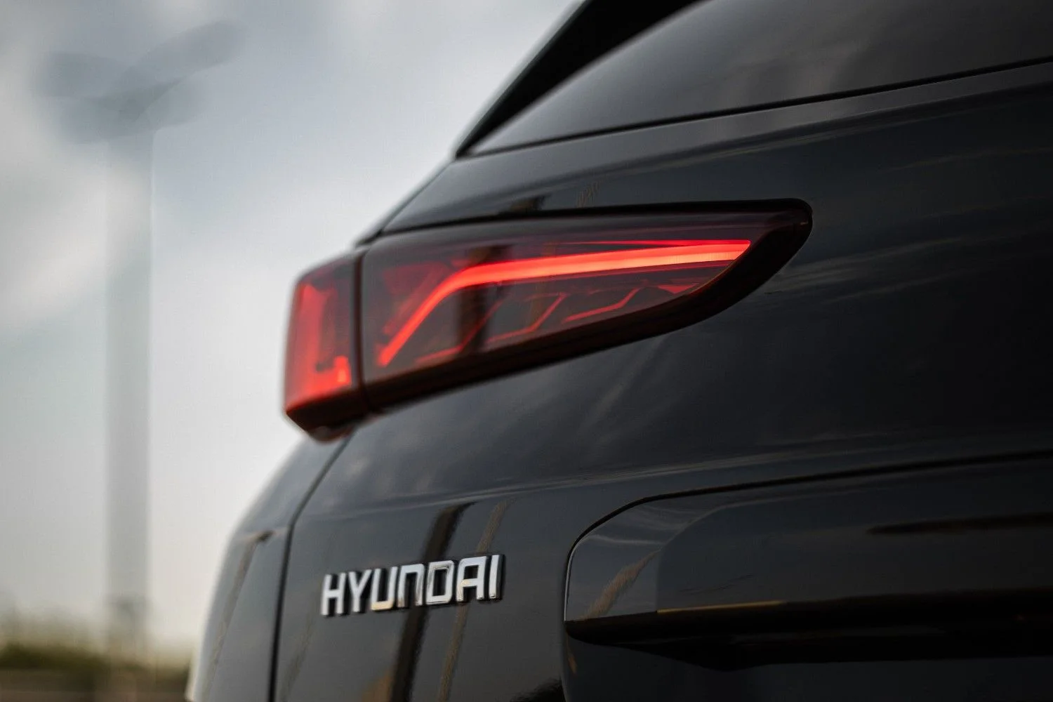 Close-up of a Hyundai car's sleek rear design featuring a modern taillight and logo against a blurred background.