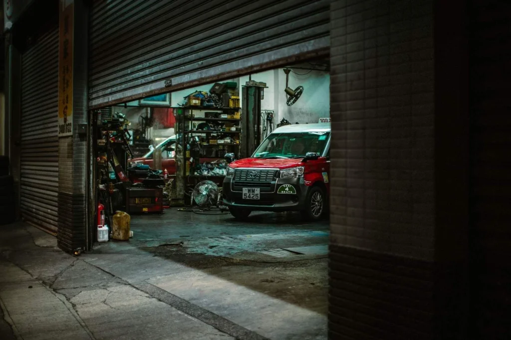 Red van inside an auto repair shop with open roller shutter, showcasing tools and equipment.